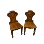 A pair of Victorian mahogany hall chairs - the shaped backs incorporating a vacant shield above