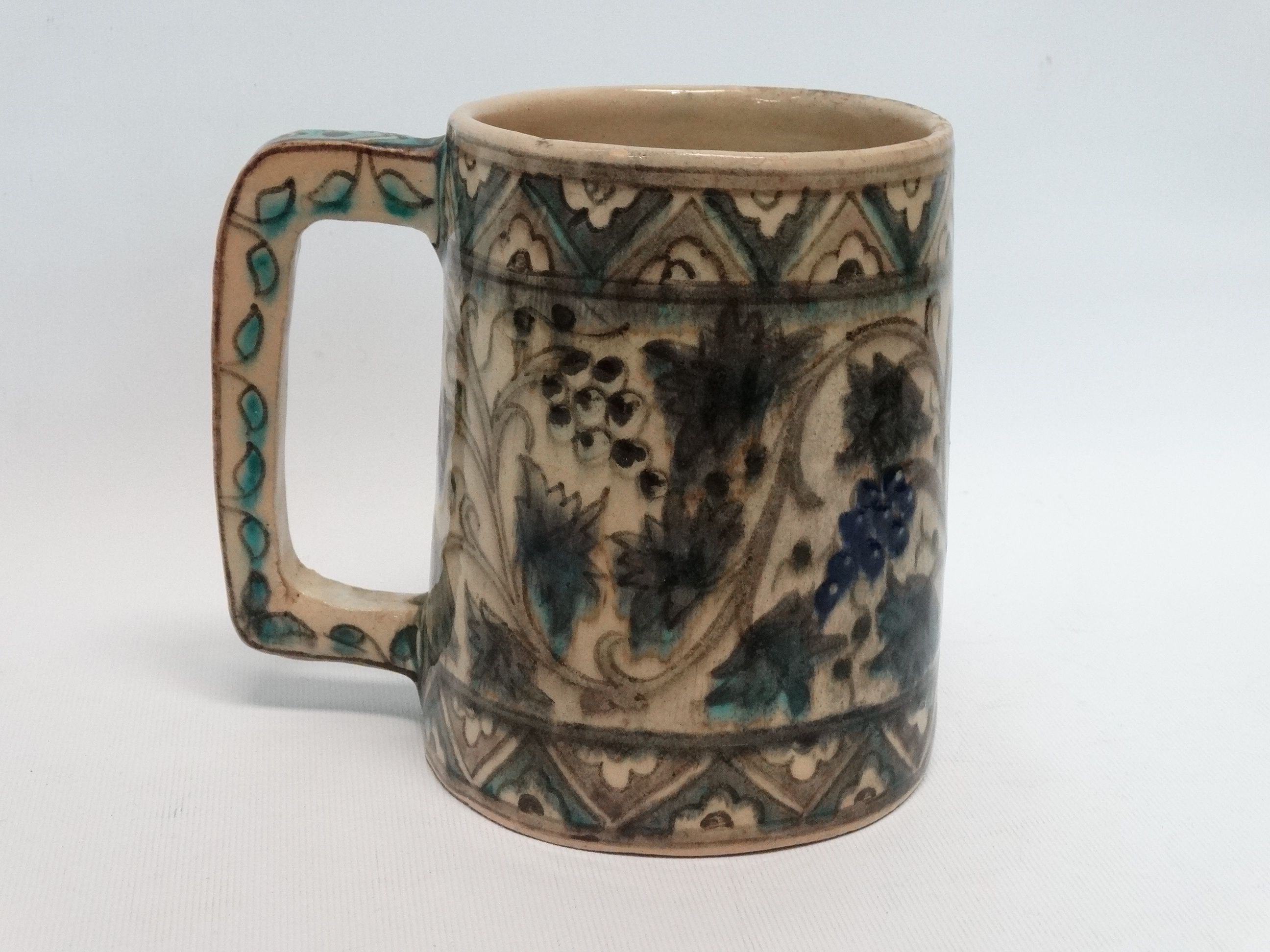 An Iznic glazed mug - decorated with vines within a geometric border, height 15cm.