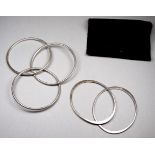 A pair of silver bangles of oval form - together with another bangle of three interlinked hoops.