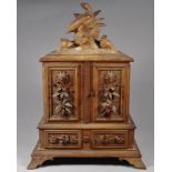 A 20th century Black Forest table cabinet - the surmount carved with pheasants above a pair of