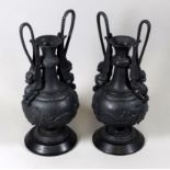 A pair of cast metal urns after the antique - decorated with dragon handles and raised on a black
