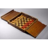 An early 20th century walnut cased travelling chess set - the turned boxwood pieces in red and