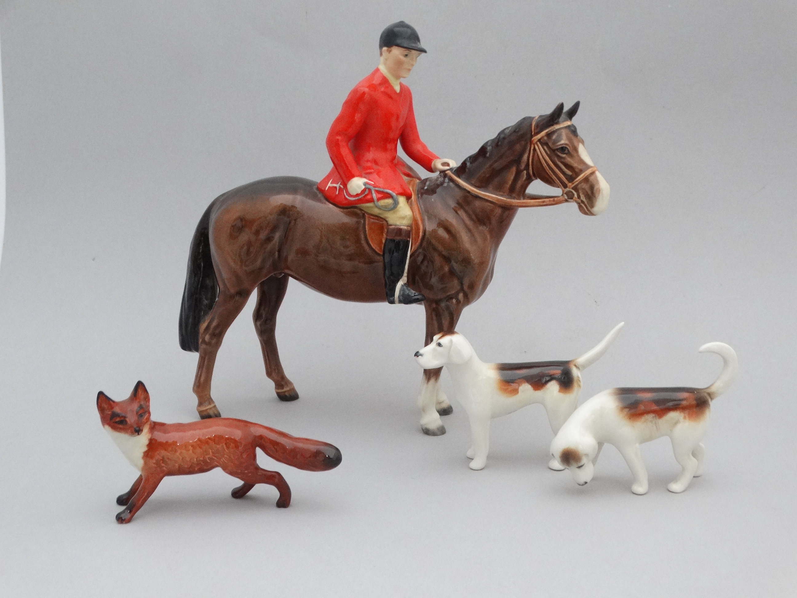 A Beswick huntsman - mounted and wearing a red jacket, height 20cm, together with two hounds and a