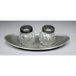 A white metal condiment tray - strike mark to rim, with two cut glass pots, width 12cm.