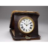 An early 20th century leather cased travelling clock - with a white enamel dial set out in Roman