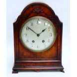 An early 20th century walnut cased mantel clock - the shaped arched case raised on bracket feet, the