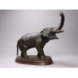 An early 20th century spelter model of an elephant - trunk raised, holding a breadfruit, on an