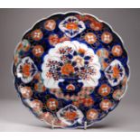 A late 19th century Imari plate - decorated with a vase of flowers within a scalloped border,