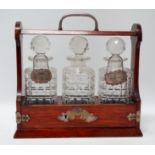 An Edwardian oak tantalus - fitted with three square cut glass bottles, with two silver bottle