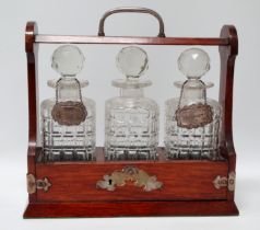 An Edwardian oak tantalus - fitted with three square cut glass bottles, with two silver bottle