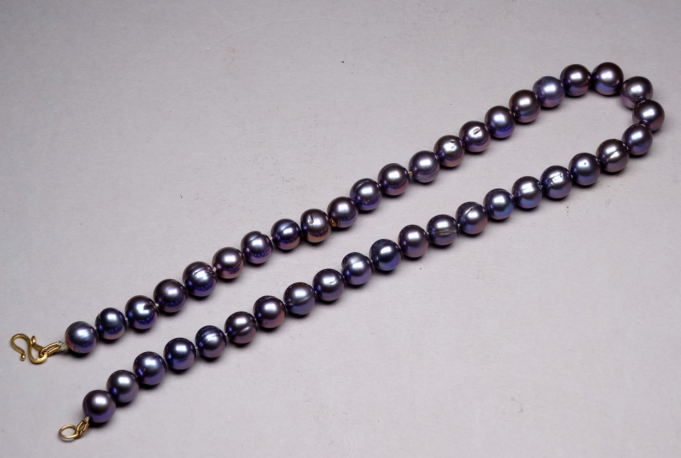 A string of uniform black Tahitian pearls - with a yellow metal S shaped clasp, possibly 9ct.