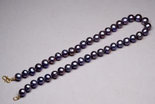 A string of uniform black Tahitian pearls - with a yellow metal S shaped clasp, possibly 9ct.