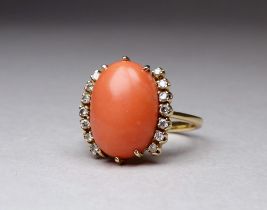 An 18ct yellow gold coral and diamond dress ring - the cabochon polished oval stone flanked by