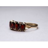 A 9ct yellow gold five stone garnet ring - claw set oval stones, ring size R-S, weight 2.6g.