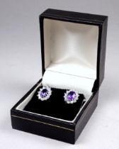 A pair of amethyst and cubic zirconia ear studs - the central oval stones within a claw set band,