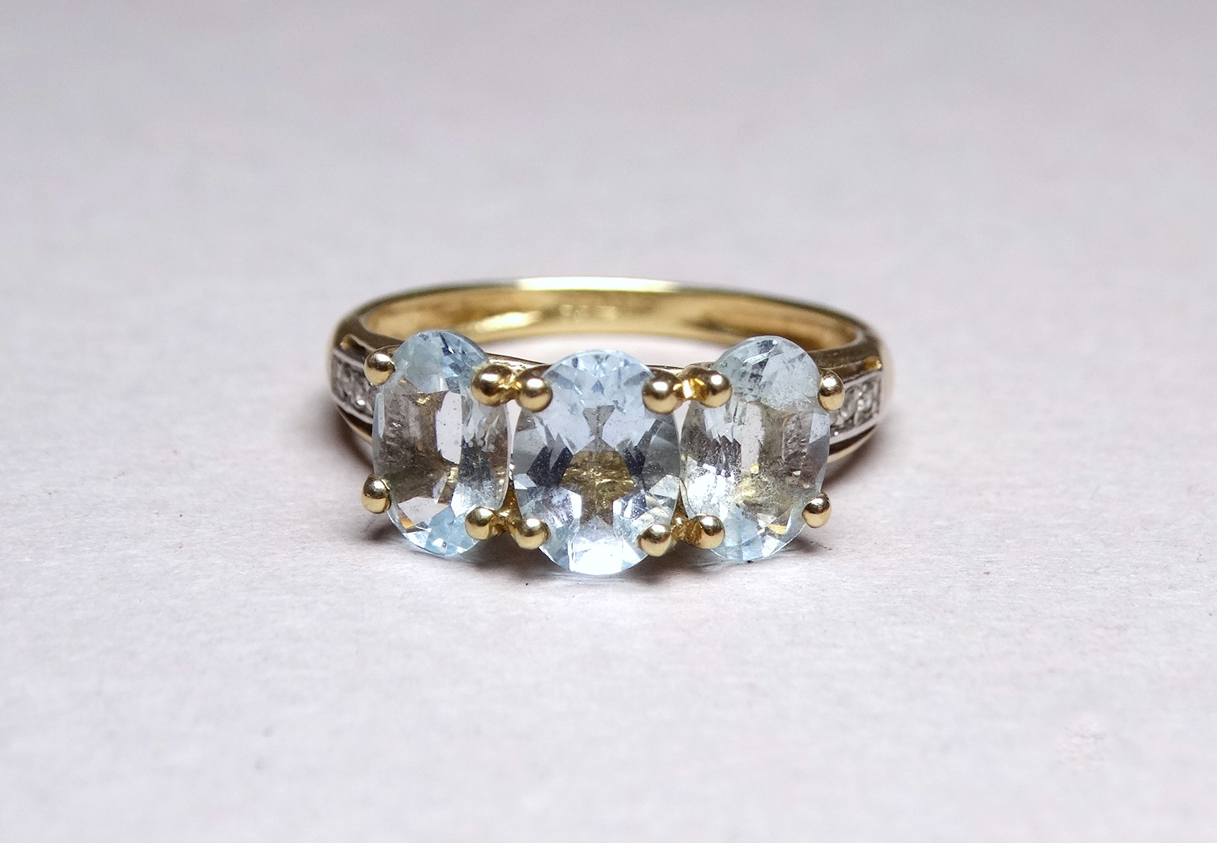 A three stone 9ct yellow gold dress ring - the aqua coloured stones claw set with diamond studded