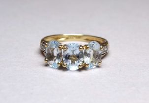A three stone 9ct yellow gold dress ring - the aqua coloured stones claw set with diamond studded
