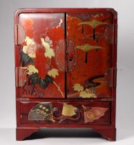 An early 20th century Japanese red lacquer table cabinet - with a pair of panelled doors enclosing