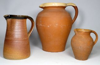 A large terracotta jug with a cream slip glaze to lip and handle - height 29cm, together with two