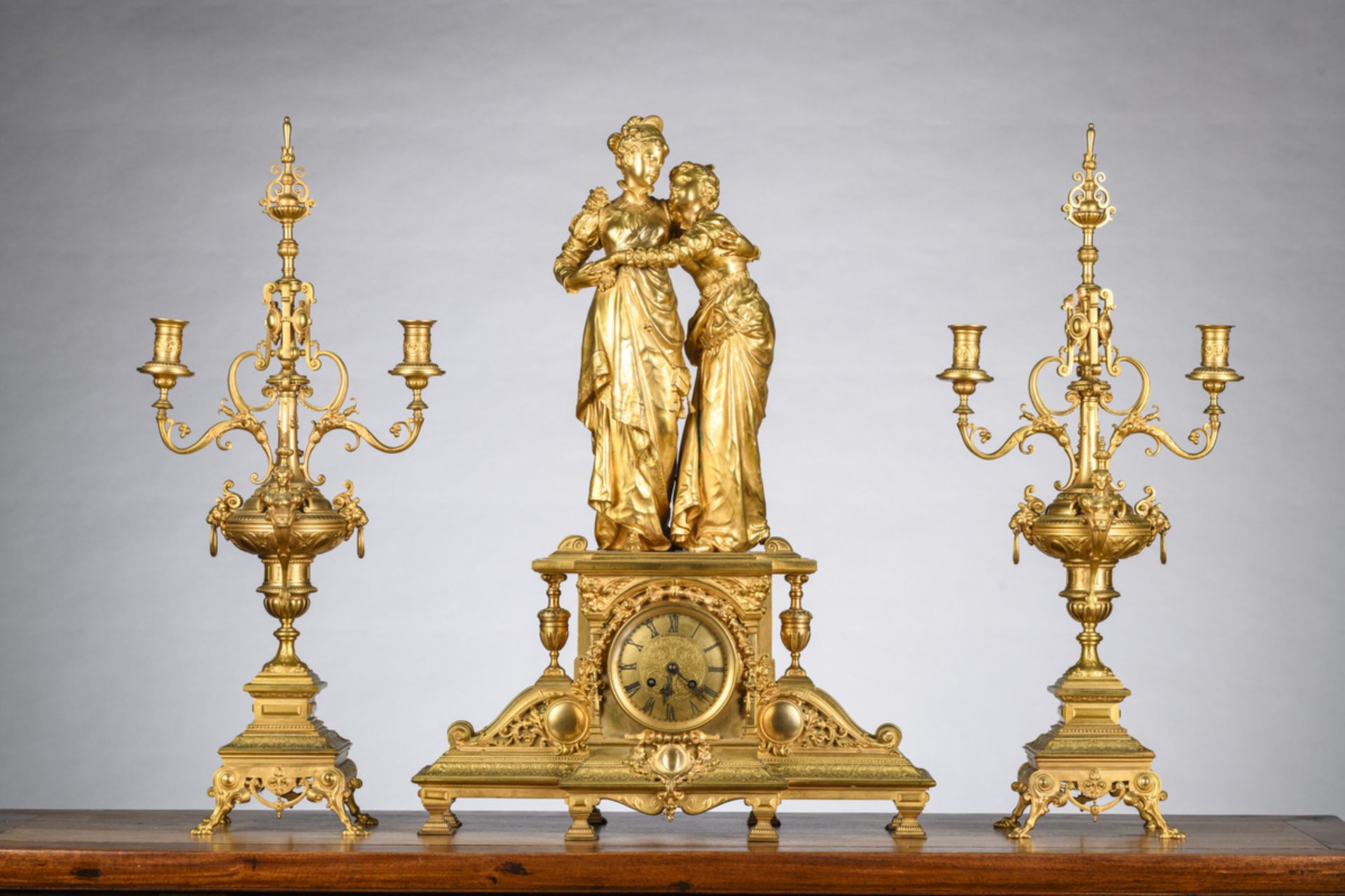 A gilt bronze clock 'ladies' by Houdebine (69x49x19cm) and two candlesticks (h68cm)