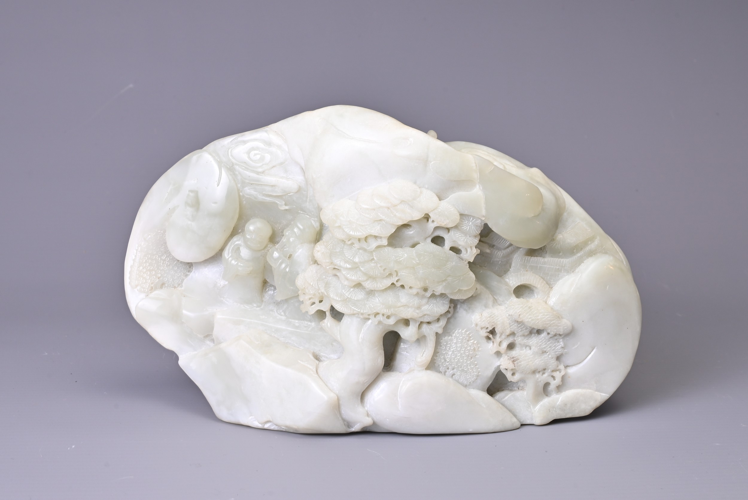 A CARVED PALE JADE BOULDER. Carved with two figures standing on pierced rockwork and trees, with