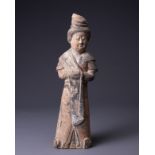 A CHINESE PAINTED GREY CARVED POTTERY FIGURE OF AN ATTENDANT, EARLY TANG DYNASTY (AD 618-907). The