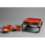 AN ASSEMBLED SET OF THREE TAISHO PERIOD (1920S) RED AND GOLD LACQUER SAKE CUPS ON STAND. In three