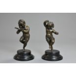 A PAIR OF BRONZE FIGURES OF PUTTI ON EBONISED BASES, LATE 19TH/EARLY 20TH CENTURY. The first cast as