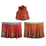 TWO CHINESE CORAL AND RED-GROUND EMBROIDERED SILK SKIRTS AND A SLEEVELESS JACKET OR VEST.