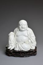 A CHINESE BLANC DE CHINE FIGURE OF BUDAI, QING DYNASTY. The figure seated dressed in robes open at