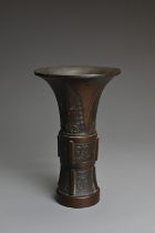 A CHINESE BRONZE GU SHAPED VASE, QING DYNASTY. Archaic decoration with Taotie masks and flanges to