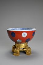 A CHINESE RED ENAMEL GROUND PORCELAIN BOWL ON ORMOLU STAND, 18/19TH CENTURY. Rounded bowl with