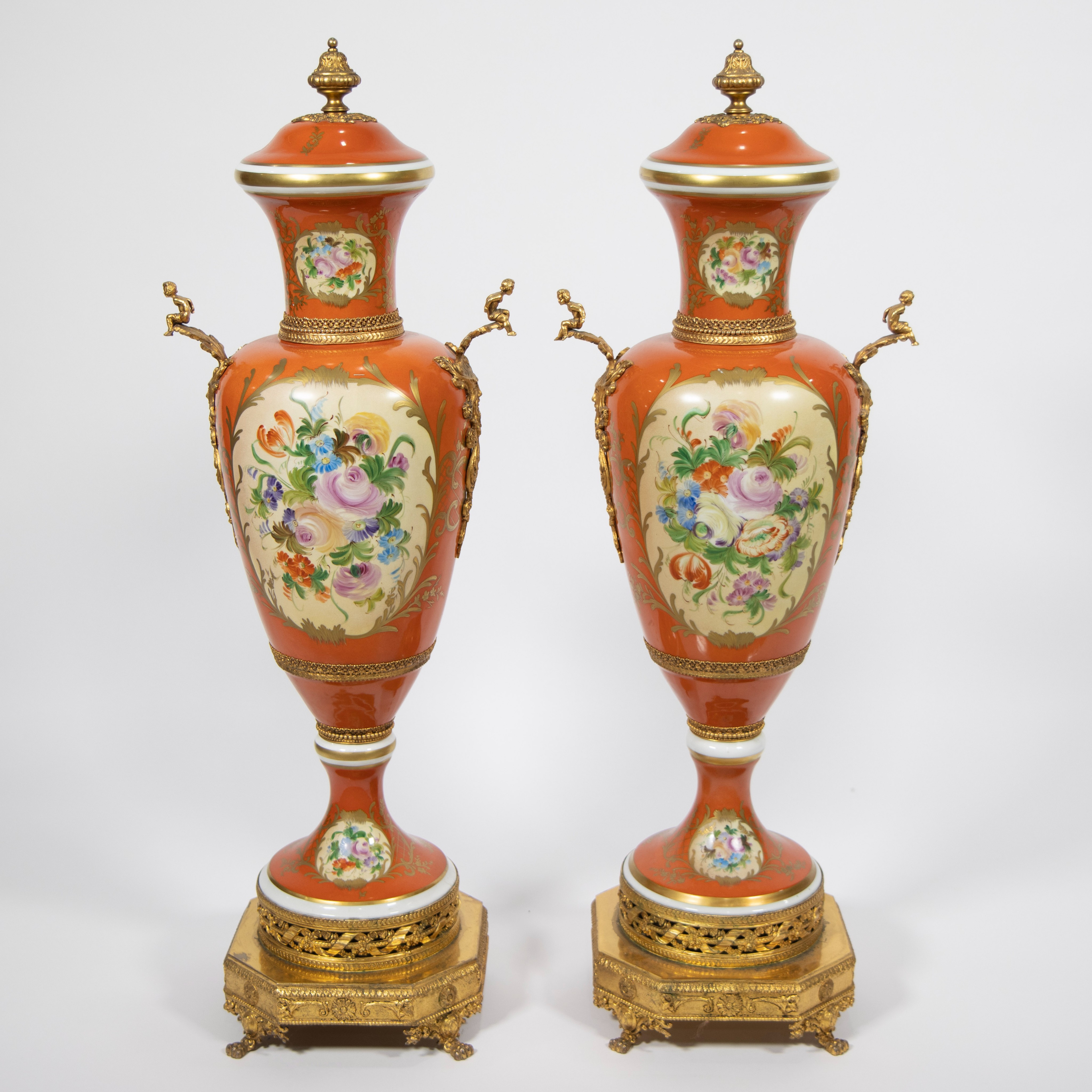 A pair of orange and polychrome porcelain covered vases with flowers and gilt bronze base and orname