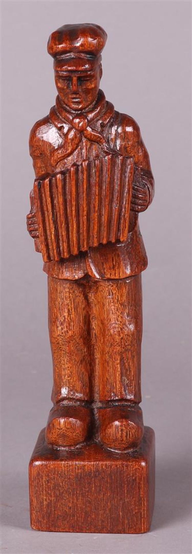 An oak sculpture of a farmer with an accordion, unclearly monogrammed in the foot.