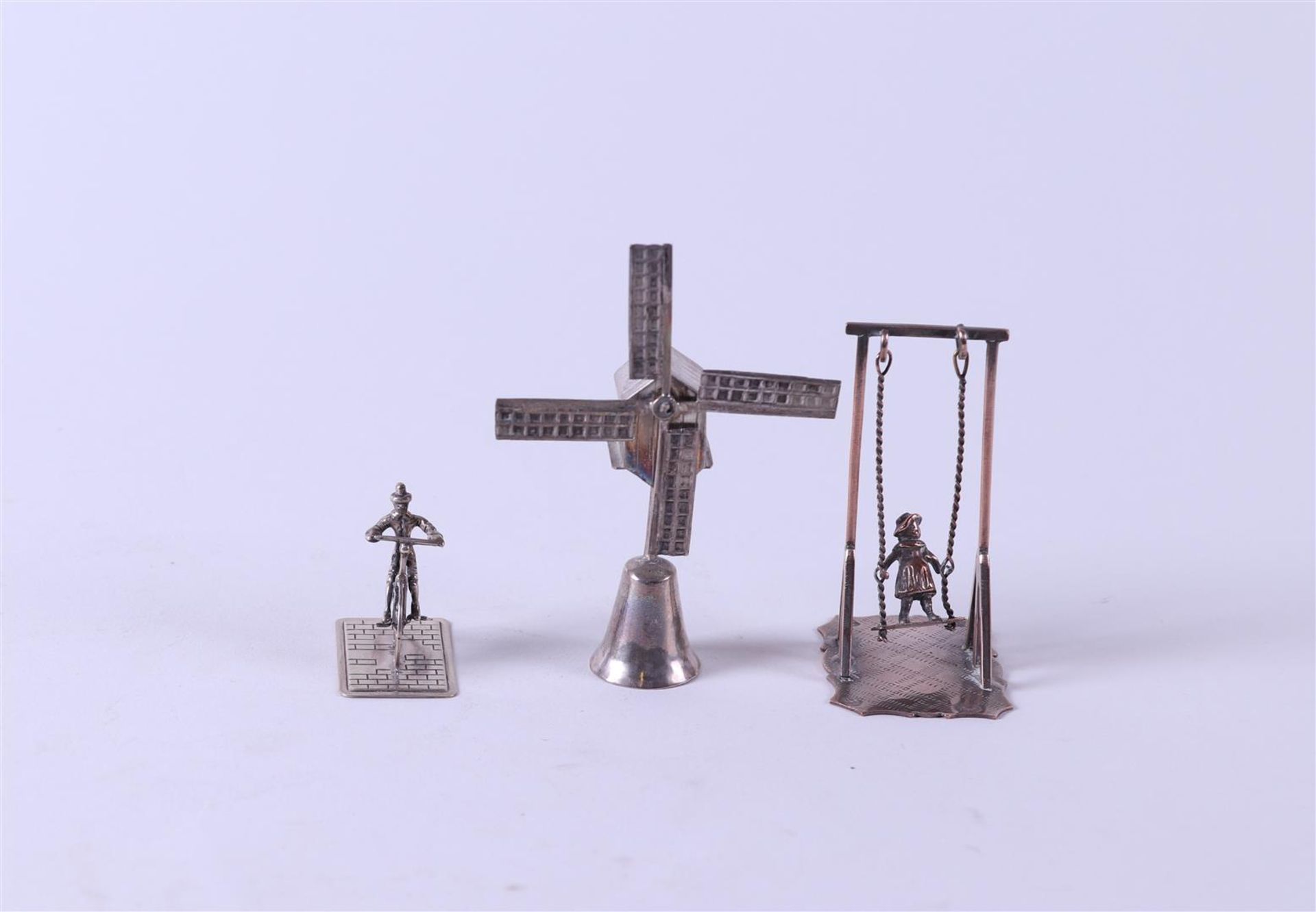 A lot comprising (3) silver miniatures, including a windmill, a cyclist, and a rocker. 76 gr.