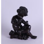 A brown patinated bronze of a writing putto. 19th century.