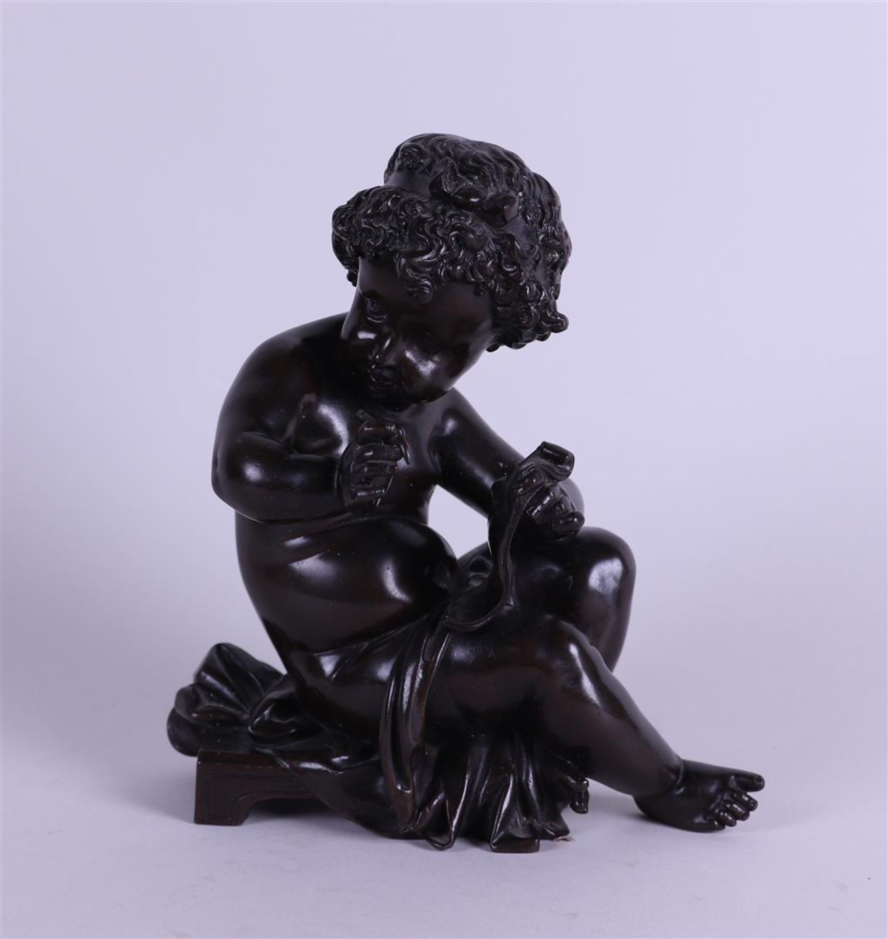 A brown patinated bronze of a writing putto. 19th century.