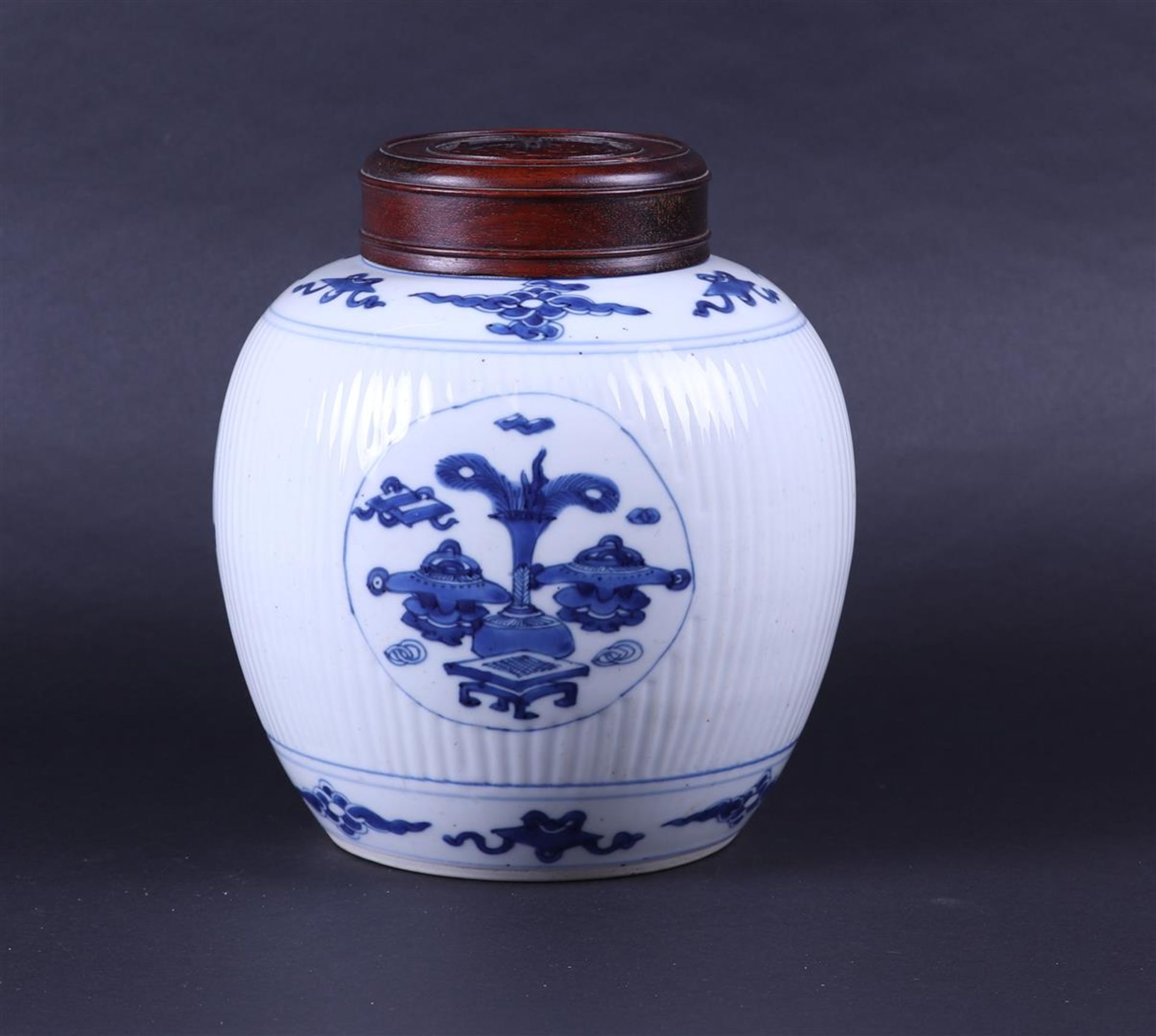 A large ribbed porcelain ginger jar decorated with various antiques and a wooden lid. China, Kanxi.