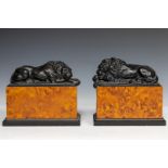 A set of cast sculptures of a sleeping lion on a faux walnut plinth, 20th century.