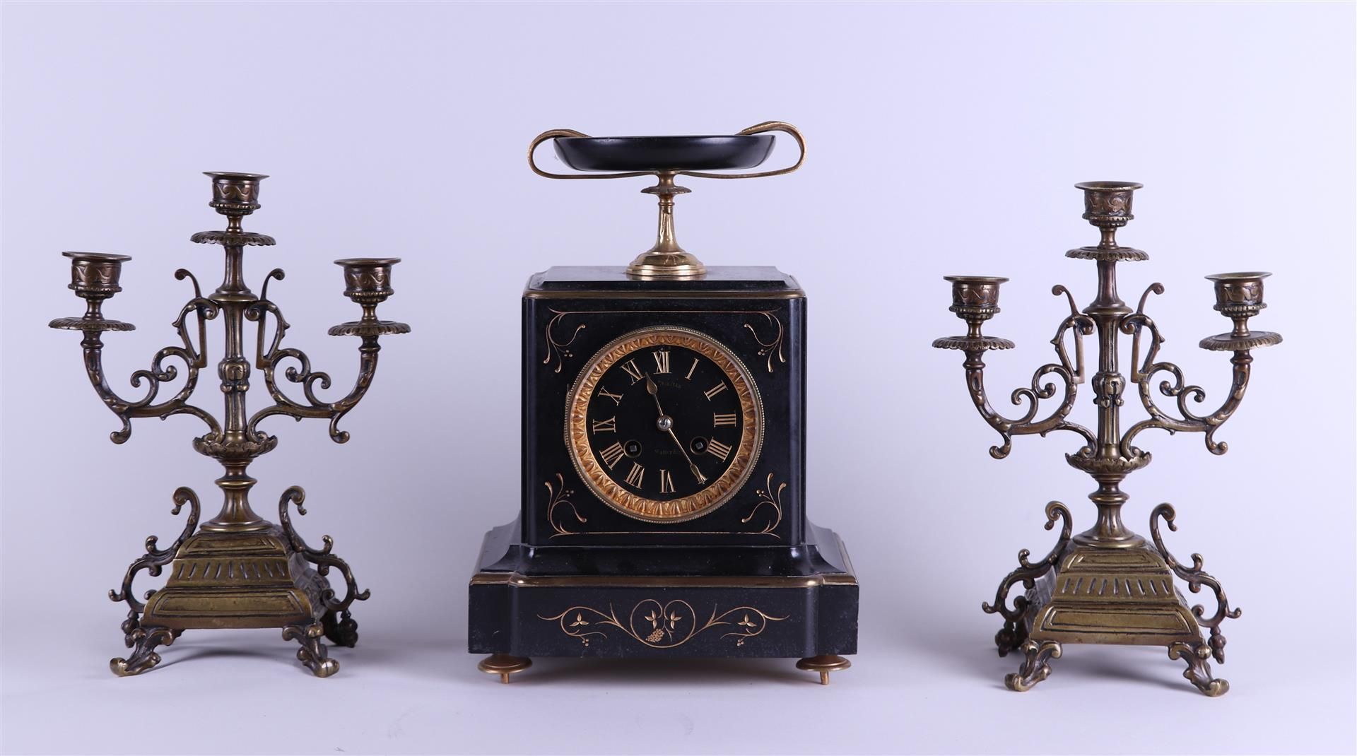 A black marble mantel clock with two brass three-armed candlesticks. Circa 1900.