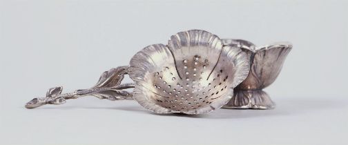 A silver tea strainer in the shape of a flower.