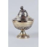 A silver lidded coupe on a round base with a constricted base surrounded by palm leaves, the lid wit