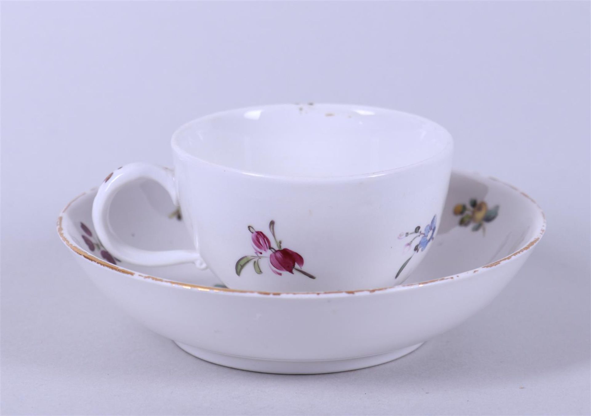 A cup and saucer with floral decor, marked on the bottom. 