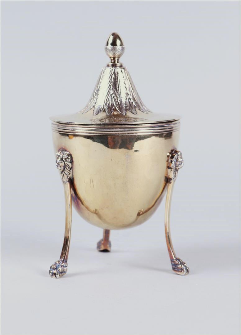 A silver lidded cup on three legs with lion masquerades, standing on claw feet, the lid with acorn-s