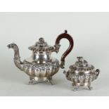 A silver teapot and sugar bowl with rich flower relief decoration on the belly and lid, the teapot w