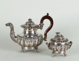 A silver teapot and sugar bowl with rich flower relief decoration on the belly and lid, the teapot w