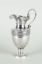 A silver jug with floral and pearl edges and a silver handle. 