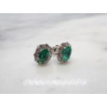 A pair of Emerald and Diamond Cluster Earrings each claw-set oval-cut emerald within a frame of
