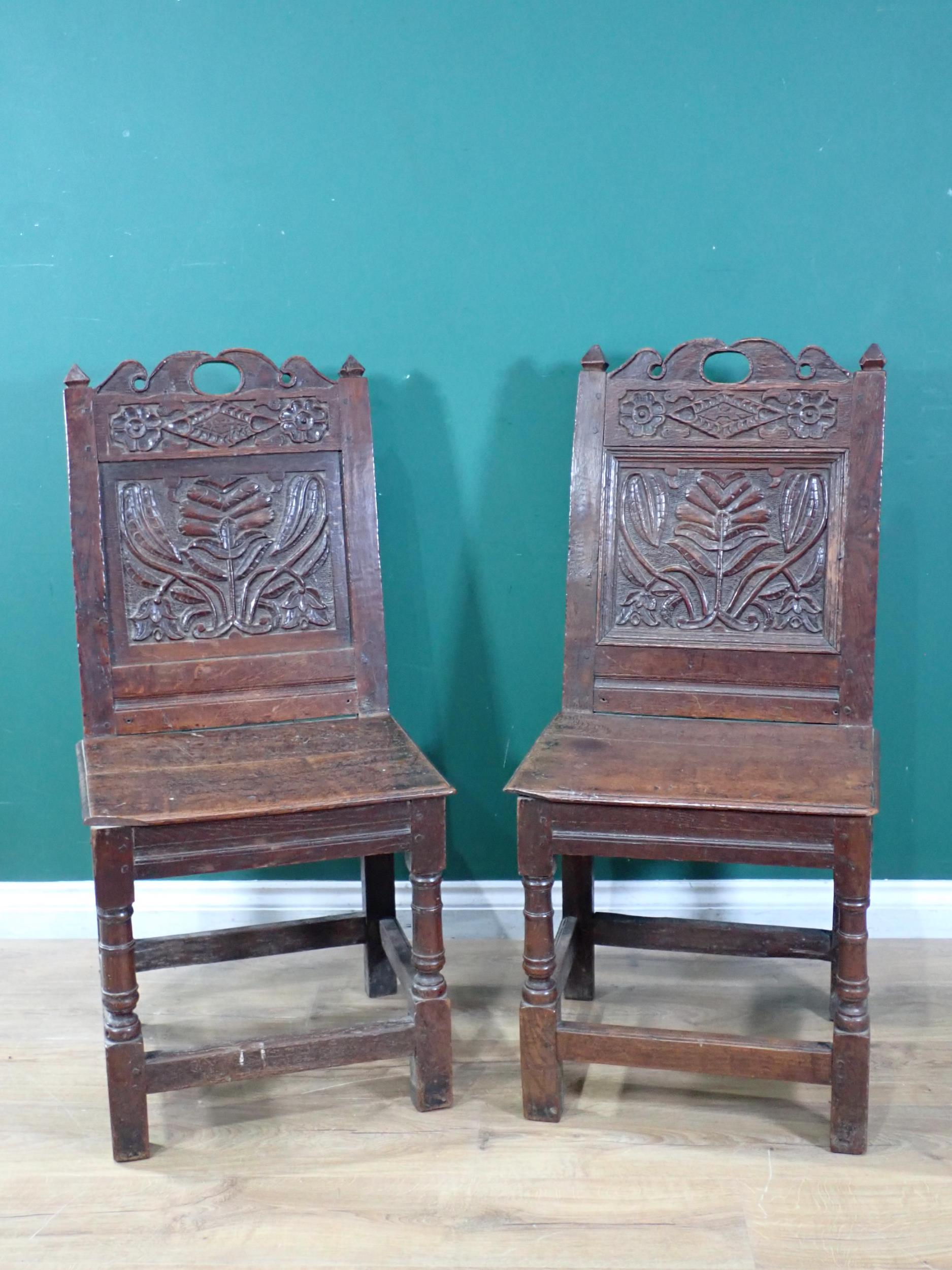 A pair of 17th Century oak Hall Chairs with pierced shaped crests above foliate carved panel