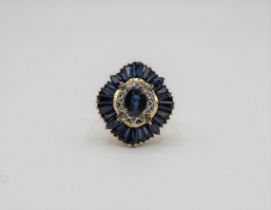 A Sapphire and Diamond Ballerina Ring claw-set oval-cut sapphire within a frame of brilliant-cut